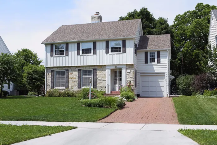 A New England colonial home with a brick driveway