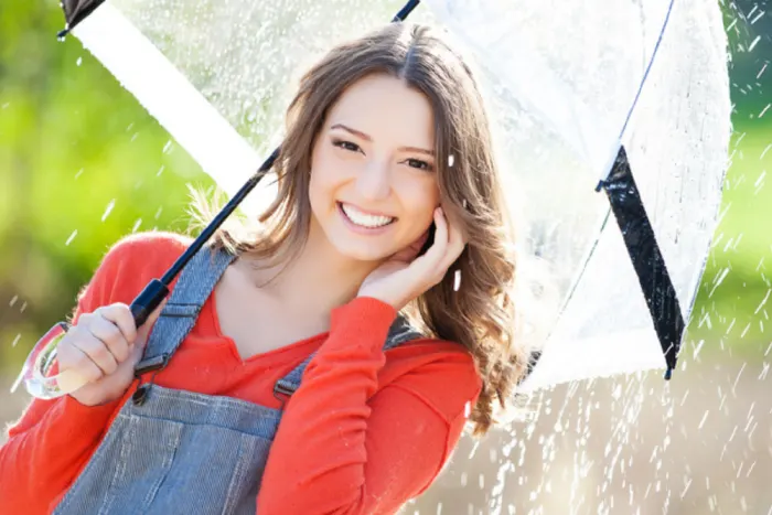 A smiling young woman holding a clear umbrella in the rain